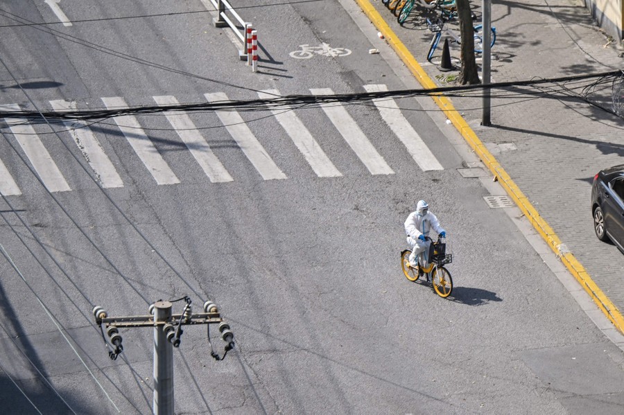 A worker wearing personal protective equipment rides a bicycle in an empty street.
