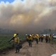 Fire scientists walk down a dirt road with a smoke-filled sky in the background.