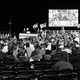 A black-and-white photo of Donald Trump speaking from a stage at a Georgia rally, taken from the perspective of a seated member of the audience.