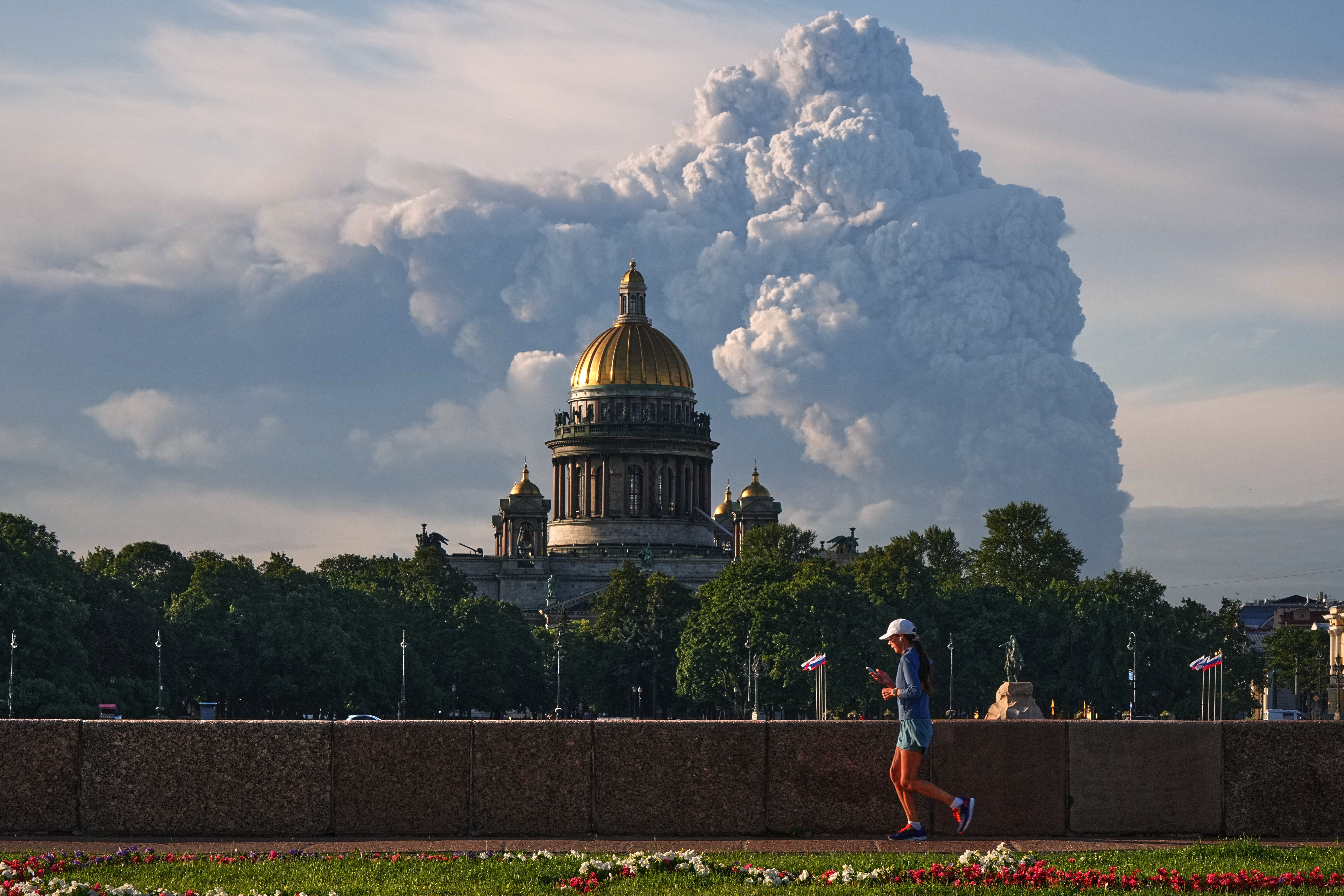 A person jogs in front of a cathedral, with a rising cloud of smoke in the background.