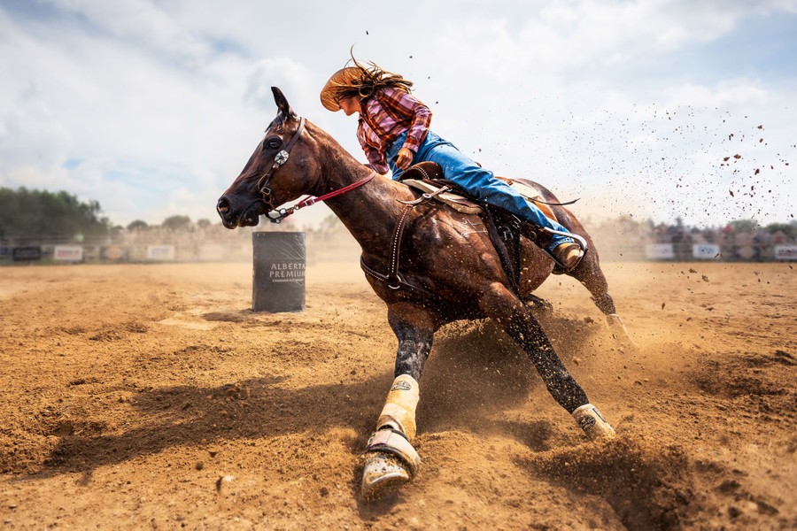 A rider on a horse makes a sharp turn around a barrel in an arena.