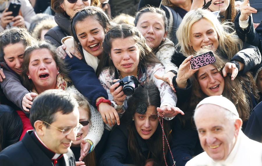 A group of young women in a crowd reach and call out as Pope Francis passes by.