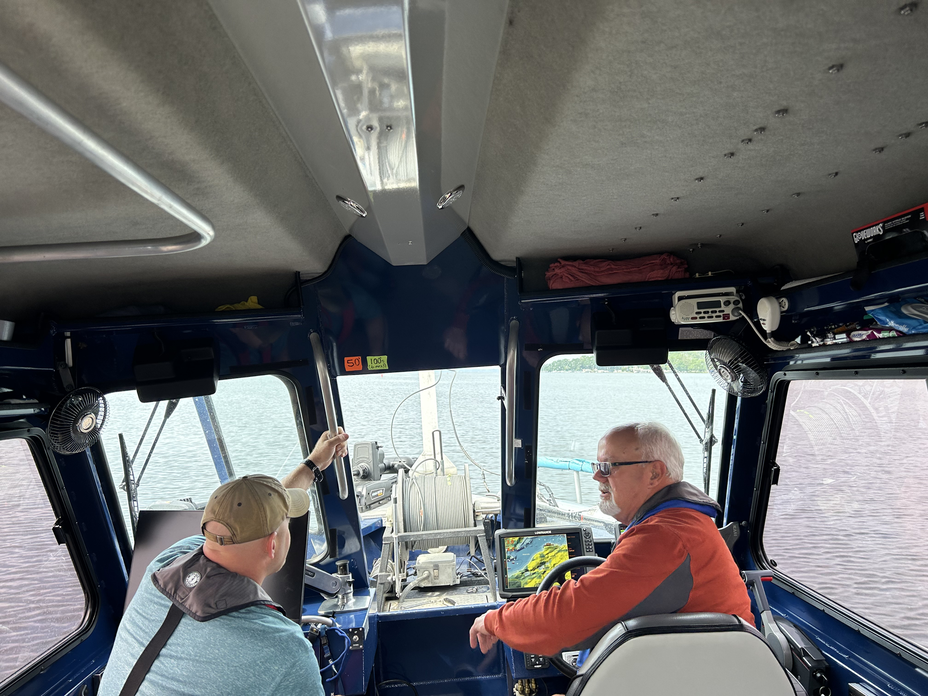 photo from inside search boat with two men sitting and talking, one at helm and the other gesturing out windshield