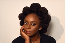 A woman looks at. camera sitting against cream wall