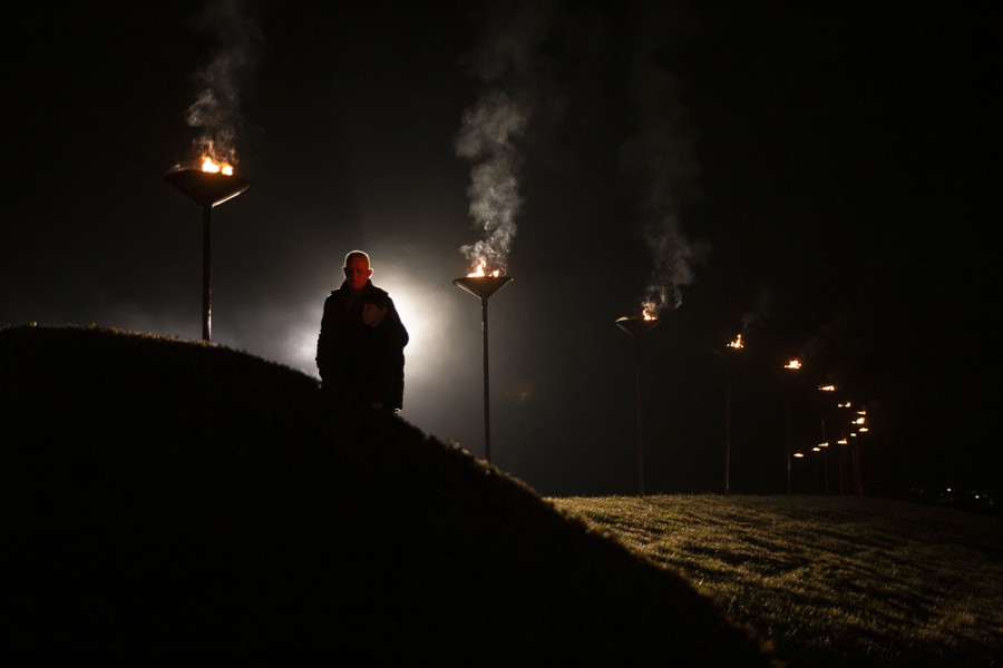 A person walks through a cemetery at night, along a torch-lit path.