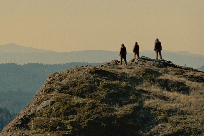 Three sasquatches standing on a cliff