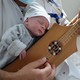 A newborn child rests on the chest of a person playing a traditional stringed instrument.