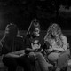 Three teenagers wearing masks look at their phones in a park