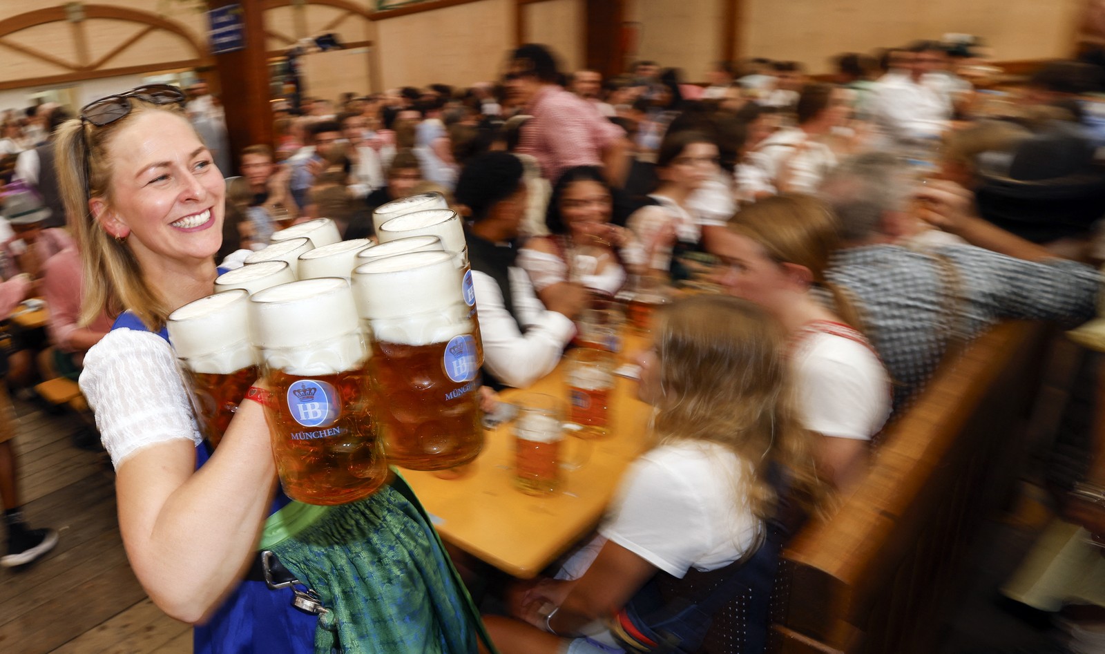 A waitress carries many beer mugs in a beer hall during Oktoberfest.