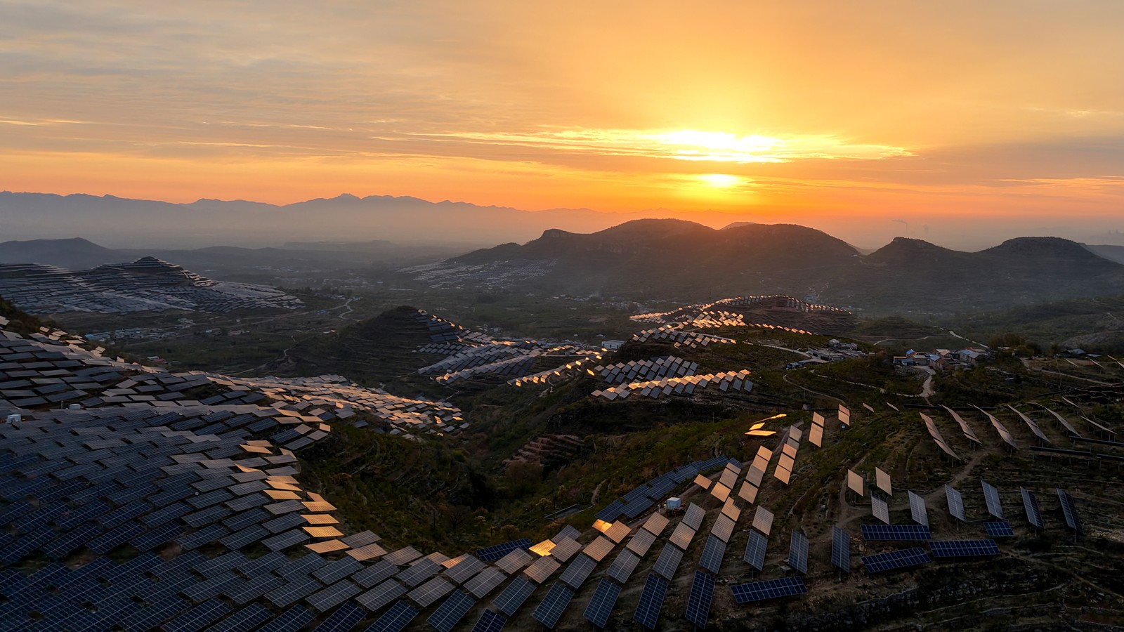 An aerial view of a sunrise over a hillside photovoltaic power installation
