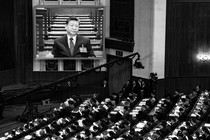 Black-and-white photograph of a crowd watching Xi Jinping speak at a podium