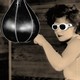 A woman in "clout goggles" (white sunglasses) hits a punching bag.