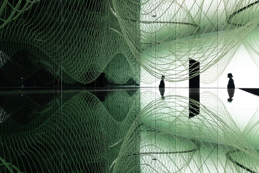 A person walks through an exhibit space dominated by a swooping sculpture that looks like a drooping grid.