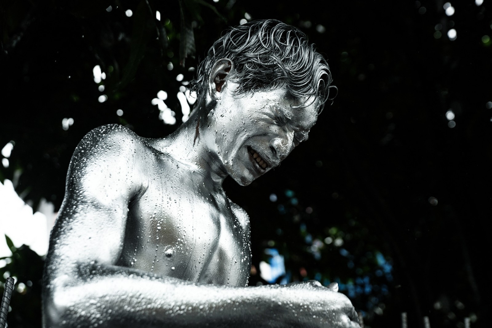 A man covered in silver paint winces, as some paint gets in his eyes.