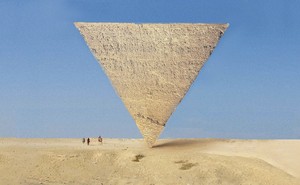 A pyramid balances on its point, upside down, in the desert with blue sky and 3 small figures