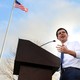 Pete Buttigieg speaks in Iowa with an American flag waving behind him and his wedding ring showing on his left hand