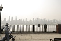 A woman pushes a stroller, with smoky air in the background