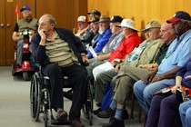 Older people wait in chairs and wheelchairs.