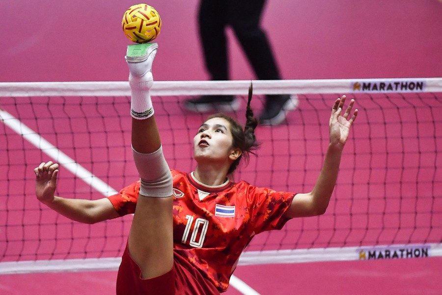 An athlete balances a ball on their foot, which is raised high above their head.
