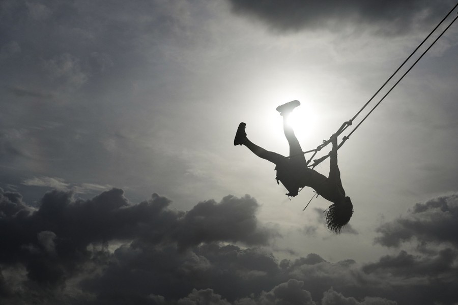 A woman swings high, leaning back, captured in silhouette.