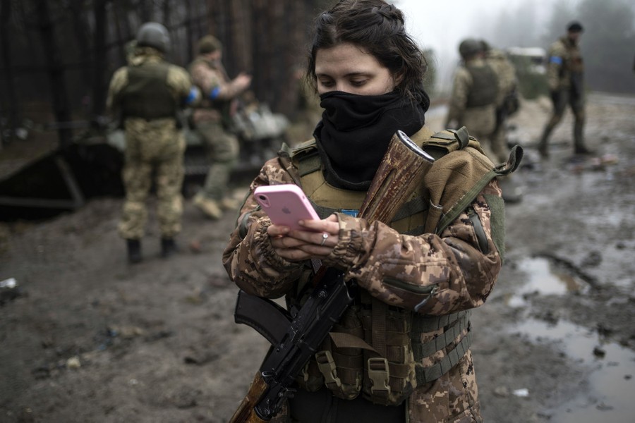 A soldier checks her phone while other soldiers stand nearby.