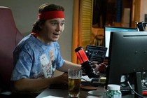 a man in a sweatband and cat tshirt sitting at desk speaking into a microphone