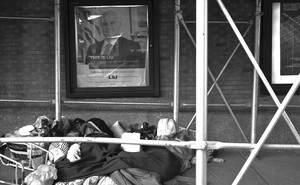 A pile of belongings on a city street, below a poster saying "This is where health executives are made"