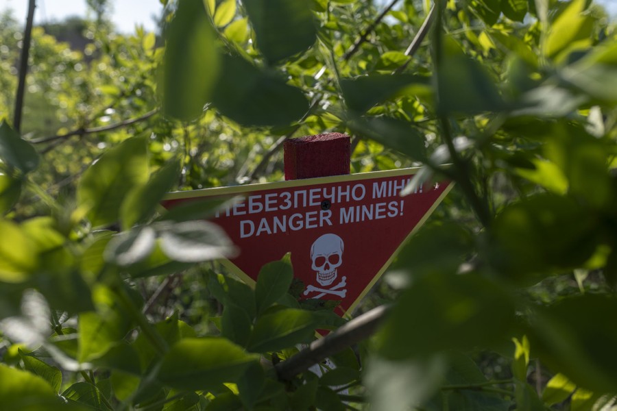 A sign warns "Danger Mines!" in both Ukrainian and English, set among bushes.