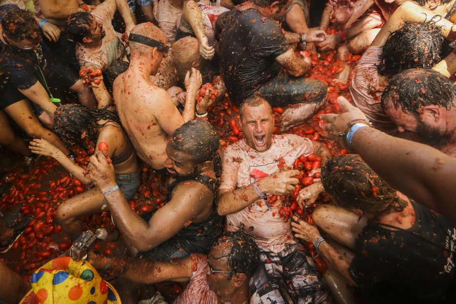 A crowd of people climb on and roll around in a pile of tomatoes.