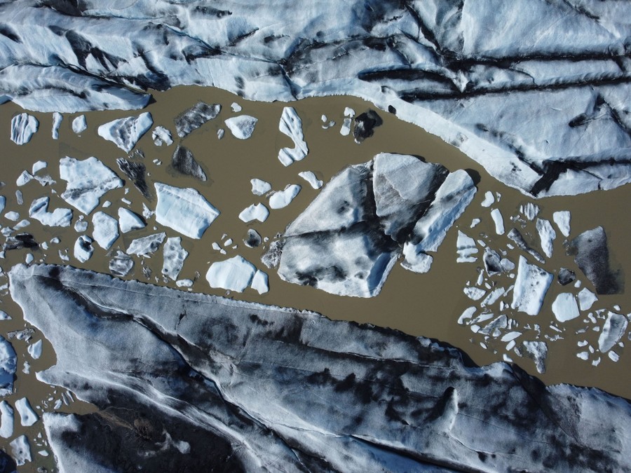 An aerial view of small and large icebergs floating in muddy water.