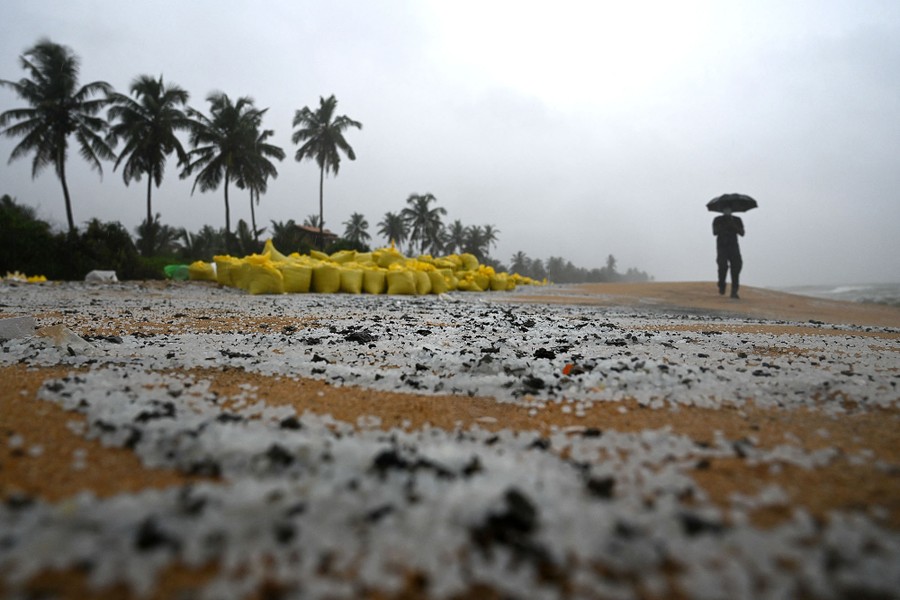 A man walks on a polluted beach past sacks containing debris.