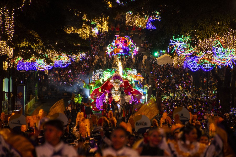 People watch and take part in a colorful holiday parade at night.