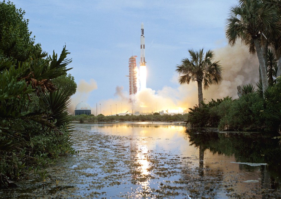 A large rocket blasts off from a pad in Florida, beside a swampy area.