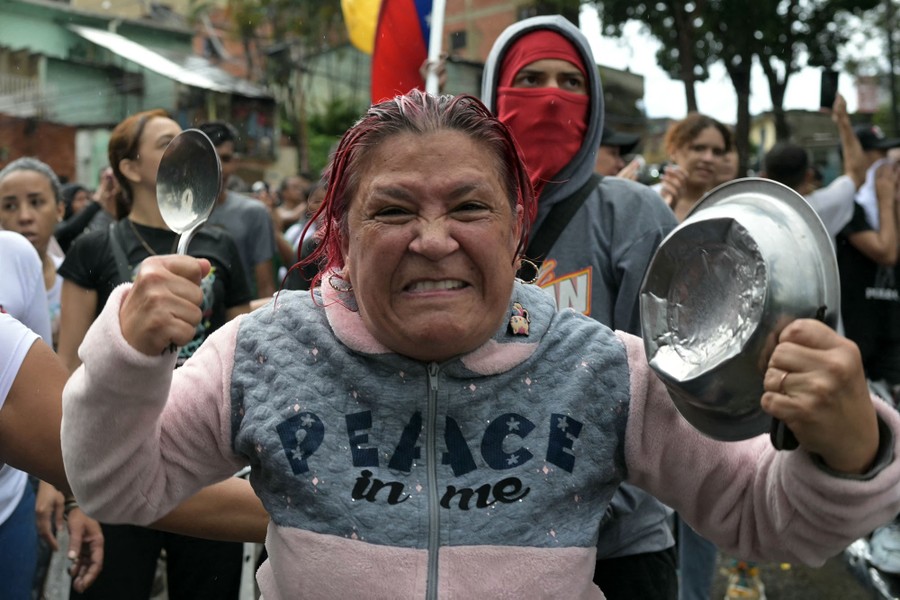 An angry person holds up a large spoon and a deeply dented metal pan during a protest.