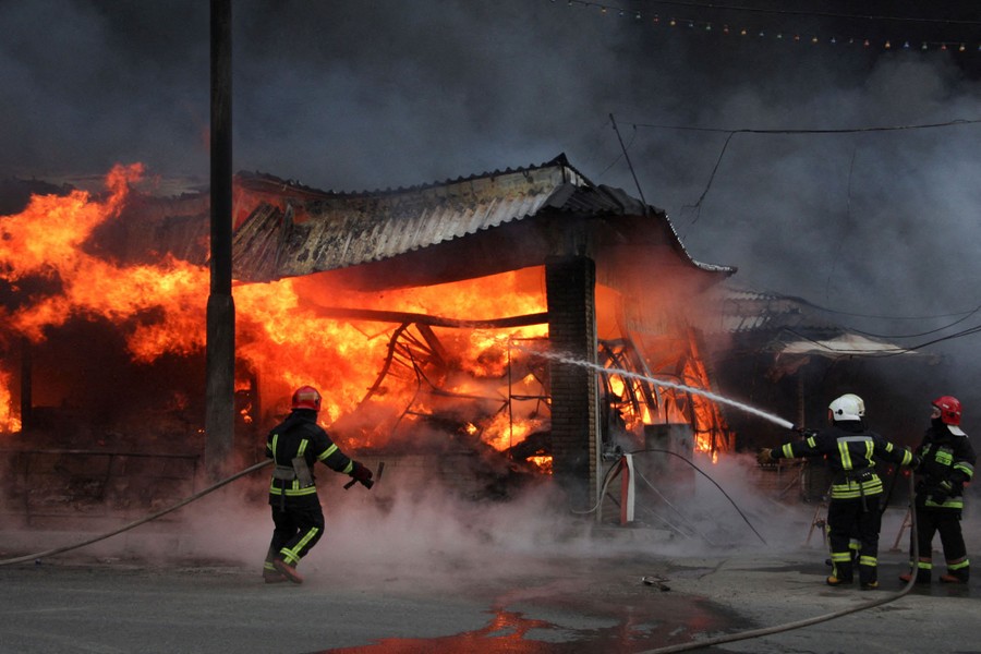 Several firefighters spray water on a raging blaze inside a market building.