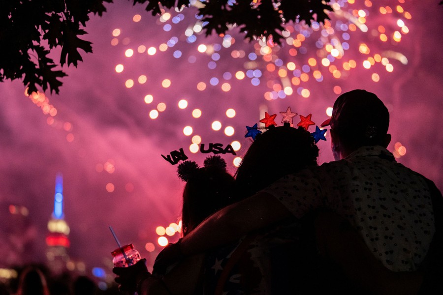 Several people in silhouette with fireworks above