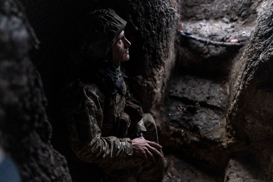 A soldier sits in a muddy trench.