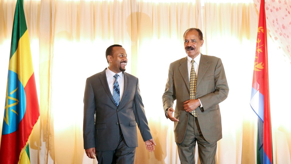 Ethiopian Prime Minister Abiy Ahmed laughs next to Eritrean President Isaias Afwerki, between flags from their two countries, at the reopening of the Eritrean Embassy in Addis Ababa.