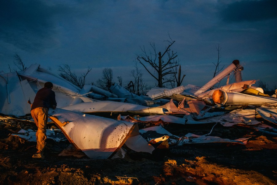 A person stands in a field among the wreckage of a water tower.