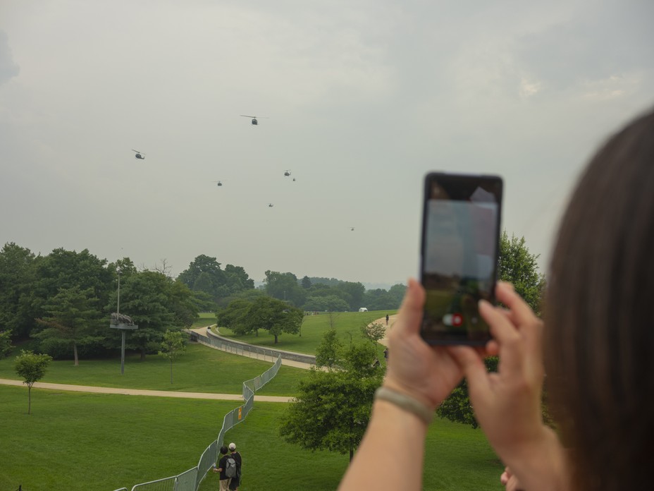 Picture of an observer photographing military helicopters flying in formation through cloudy skies. 