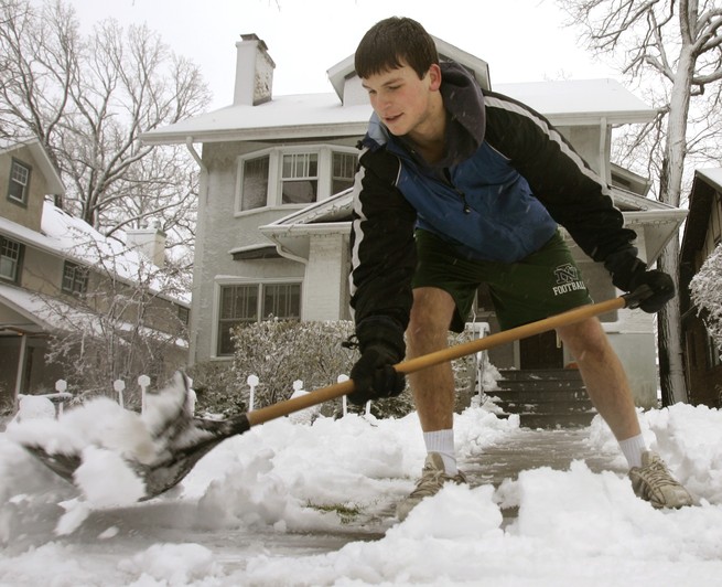 A boy wearing shorts shoveling snow.