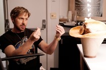 Ryan Gosling in a black T-shirt gesturing at a cowboy hat