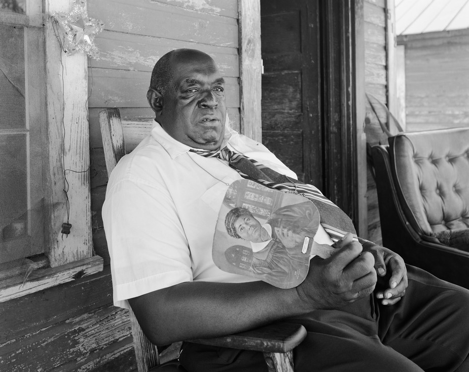 a man on a porch in a white shirt holding a fan