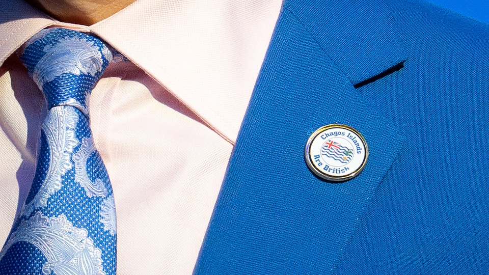 An up-close image of a suit, with a pin that reads "Chagos Islands Are British" on the blue lapel.
