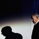 Photograph of Benjamin Netanyahu looking down with a spotlight shining on him and a shadow of himself projected on the wall behind him