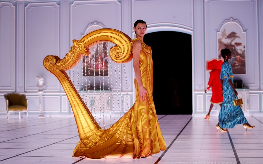 A model walks onstage wearing a costume shaped like a giant harp.