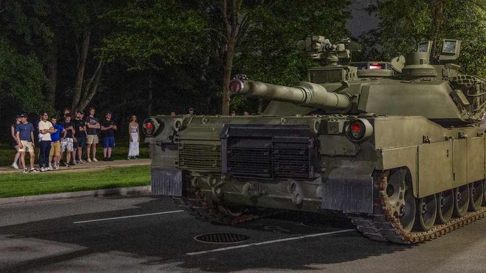 A group of young adults watches a tank roll through the street