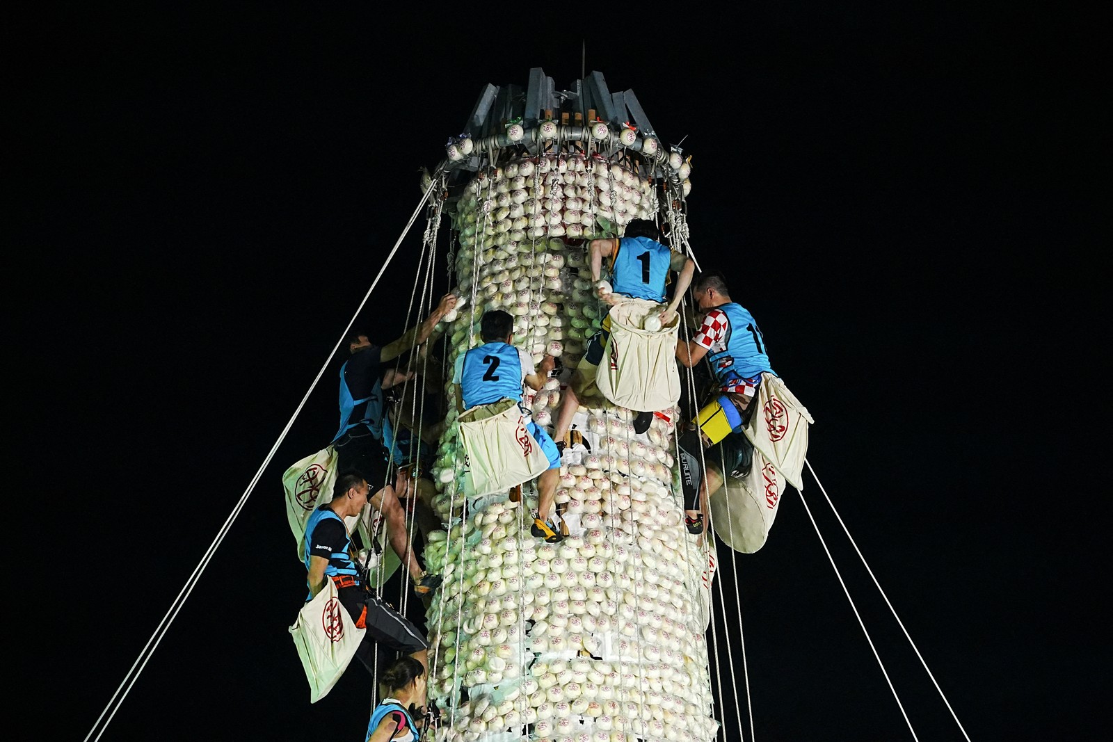 Several competitors climb up a tall pole while gathering buns that have been attached to the pole.