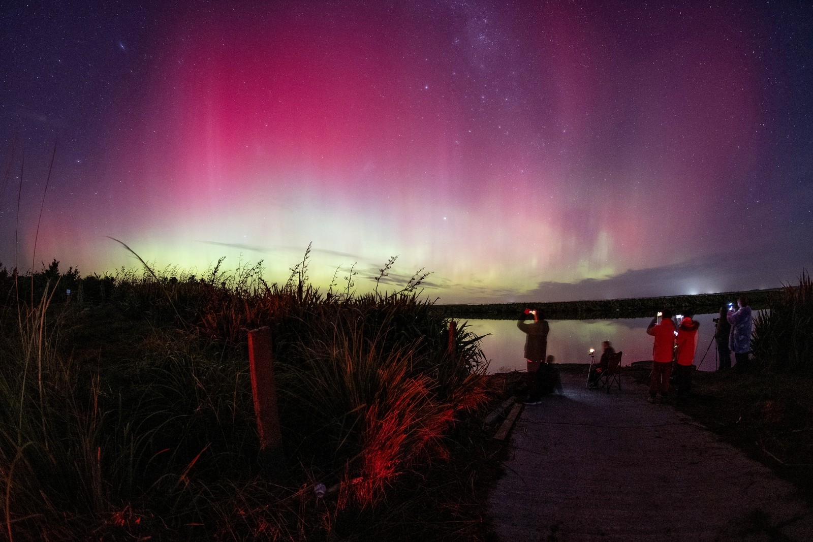 People take photos of a glowing reddish aurora in the night sky.