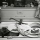 Black-and-white image of a sink overflowing with dirty dishes
